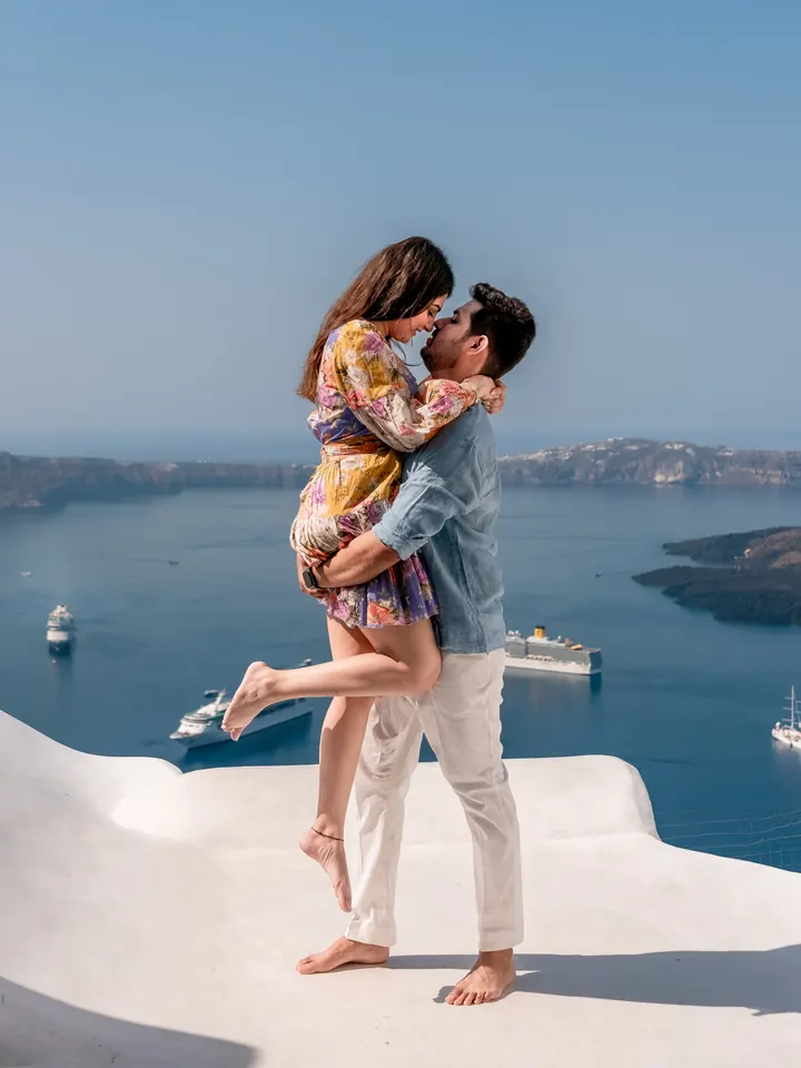 A couple laugh as he lifts her into the air on a white terrace high above the Santorini caldera